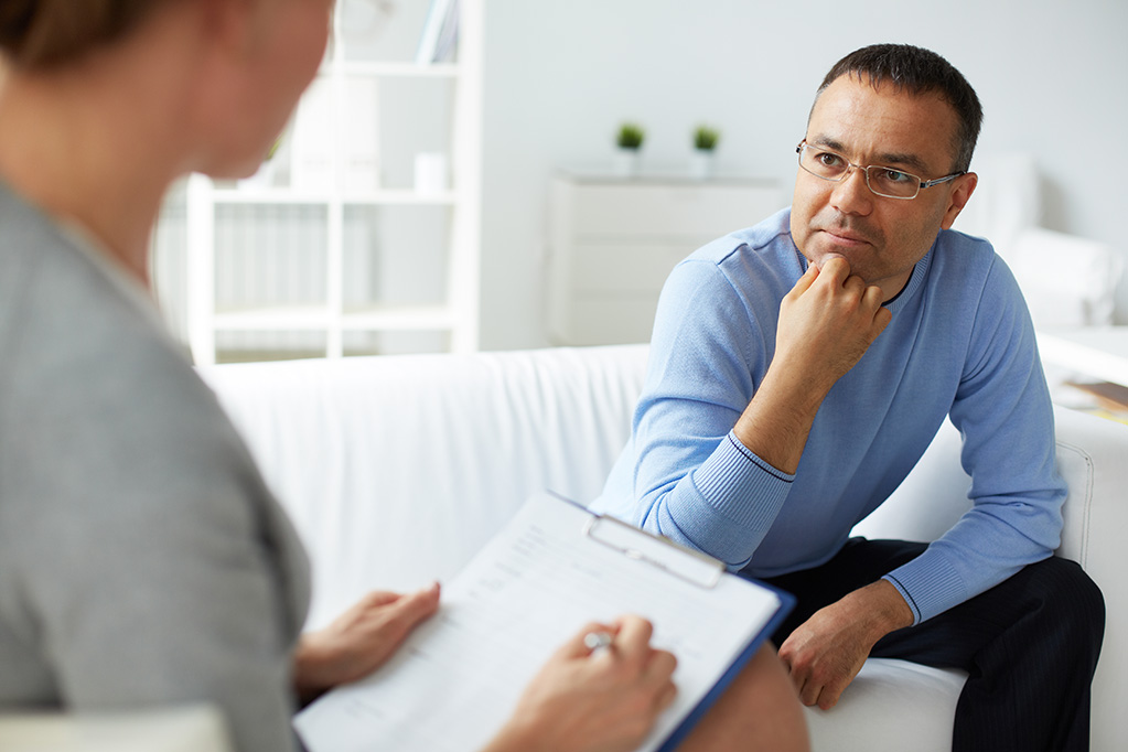 Man sitting on couch with woman with a clipboard.